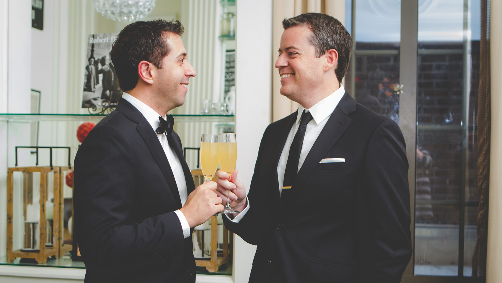 Two grooms toasting their drinks, smiling at each other