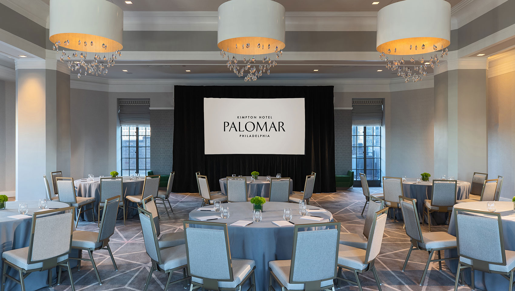Kimpton Hotel Palomar Philadelphia ballroom with crescent round tables all situated behind a projector screen and underneath 3 identical, circular lighting fixtures