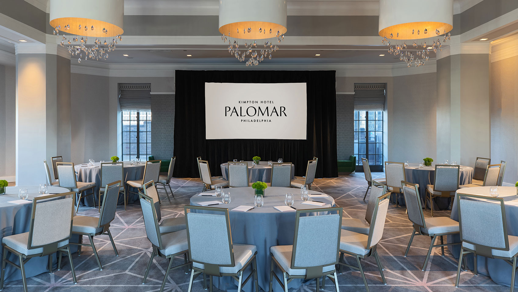 Kimpton Hotel Palomar Philadelphia ballroom with crescent round tables all situated behind a projector screen and underneath 3 identical, circular lighting fixtures